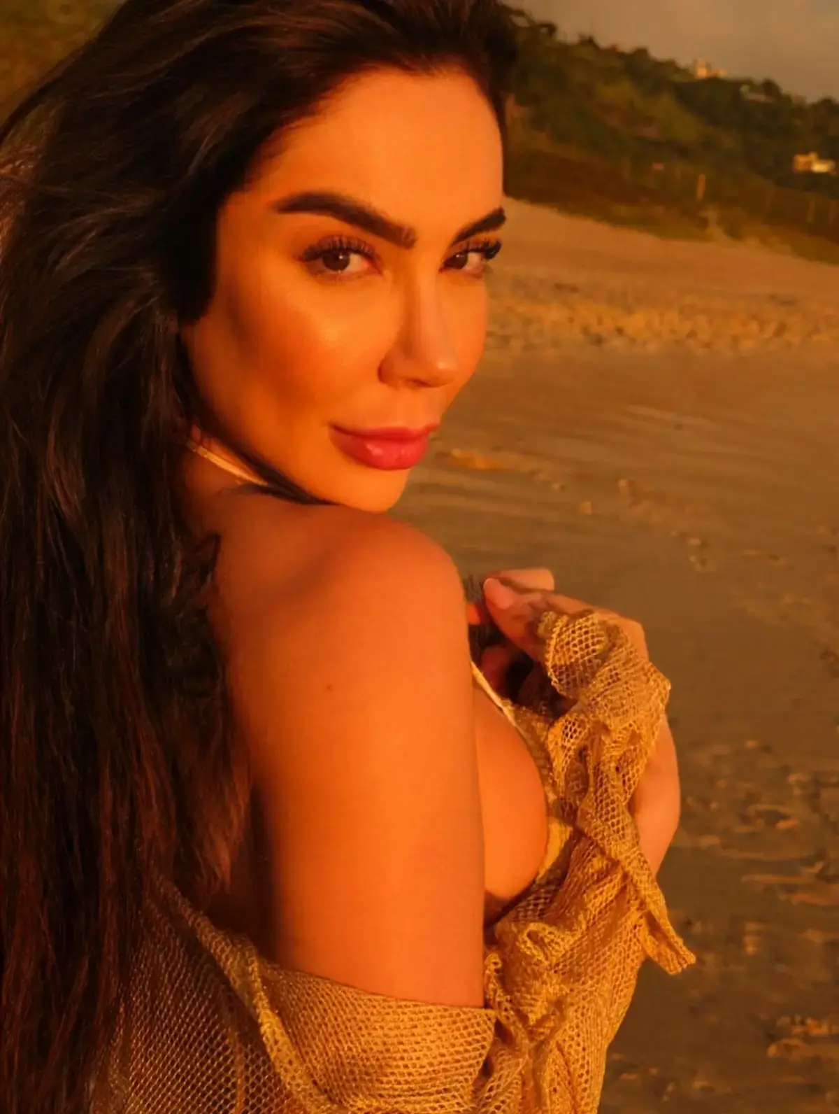 Woman with long dark hair on a beach at sunset.