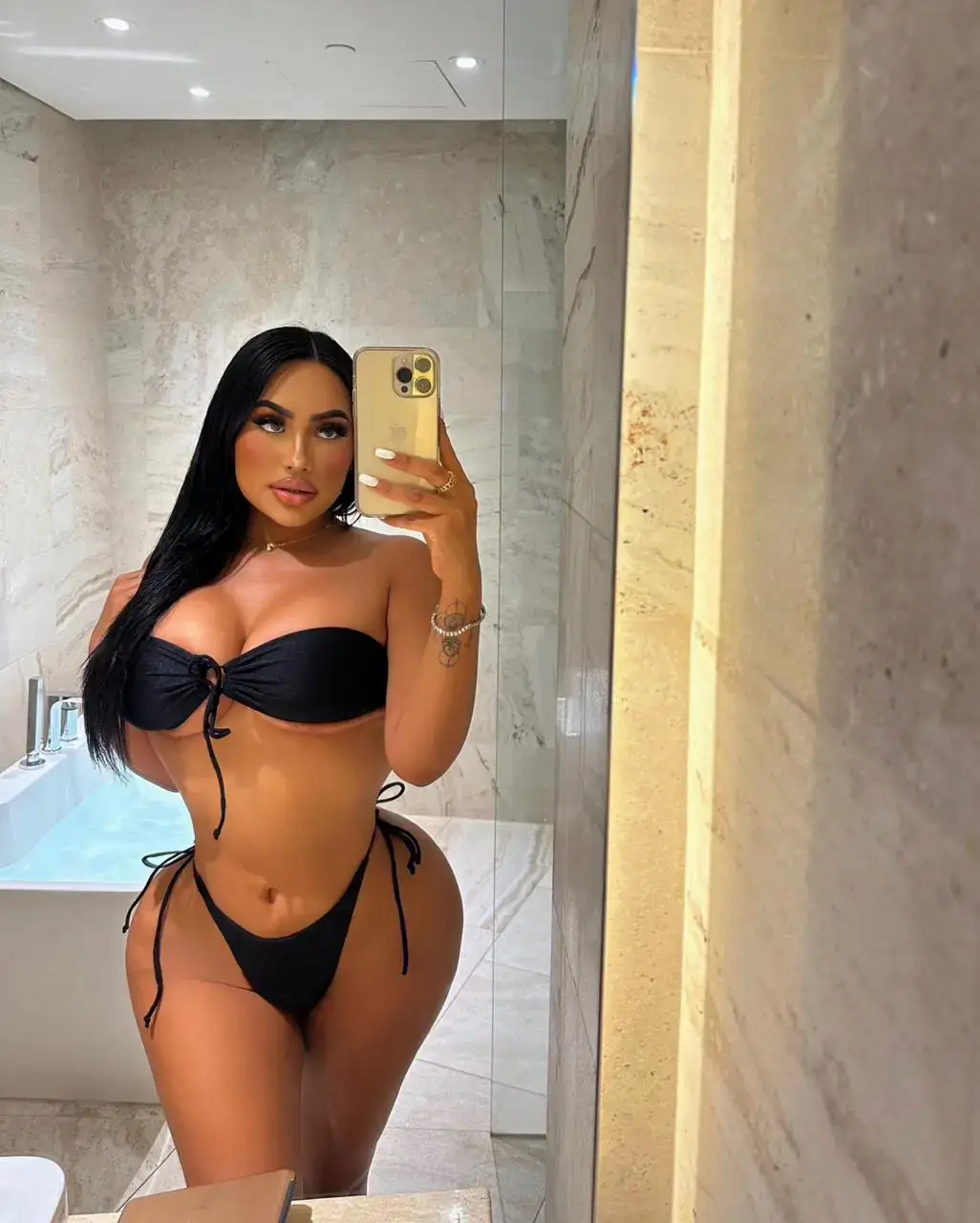 Woman in black bikini taking a mirror selfie in bathroom